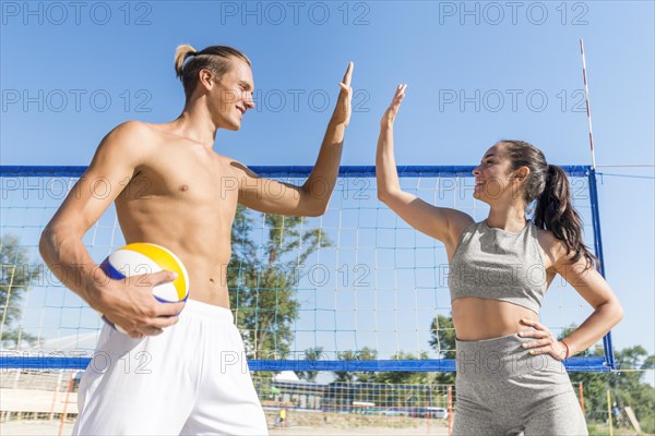 Side view man woman high fiving each other while playing volleyball