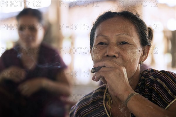 Old Burmese woman of the Bamar tribe wearing thanaka and smoking a cigar in Kayin village near Hpa-an
