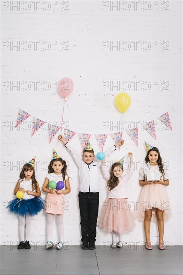 Birthday boy standing with girls against white wall decorated with bunting