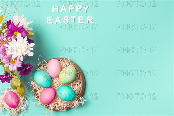 Happy easter title near bright eggs plate flower bouquet