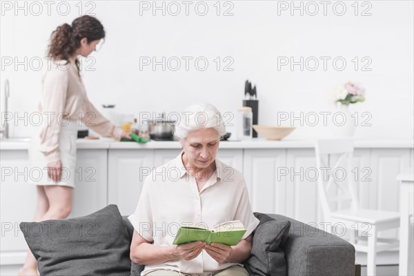 Senior woman reading book front woman doing housekeeping work