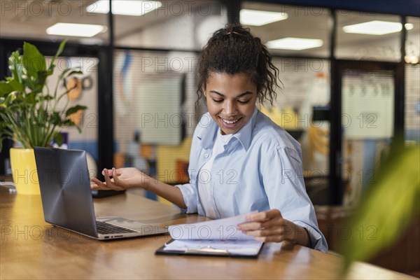 Smiley woman working office with papers laptop