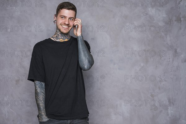 Smiling portrait tattooed young man with pierced ears talking mobile phone