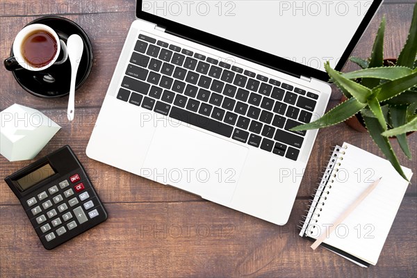 Open laptop with coffee cup spiral notebook calculator paper house model aloe vera plants wooden table