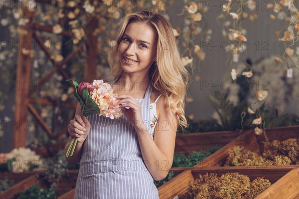 Portrait smiling blonde female florist holding flower bouquet hand