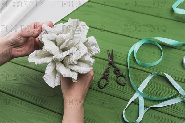 Person s hand holding fake crepe paper flower green textured background