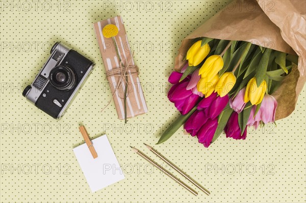 Top view retro camera blank paper pencils gift box bouquet tulip flowers yellow polka dot background