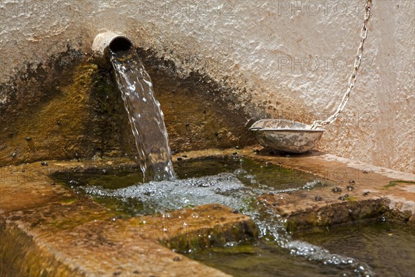 Fresh mountain water from well pouring in old fountain with stone basin to offer drinking water to people and domestic animals in village