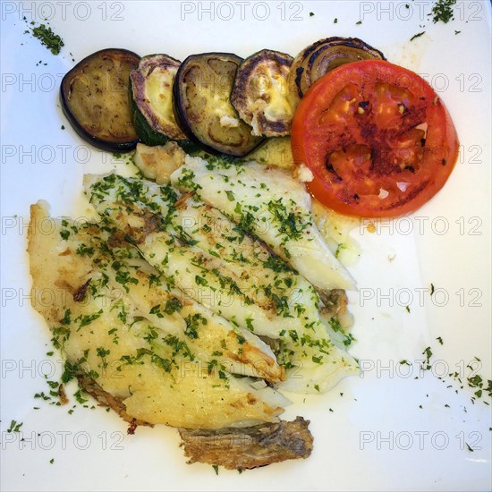 Mediterranean dish for healthy eating according to Italian recipe with sole Grilled sole fillet sprinkled with chopped parsley with lightly fried slices of aubergine Melanzane and tomato drizzled with olive oil
