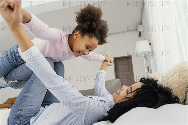 Mother playing with her smiley daughter bed home
