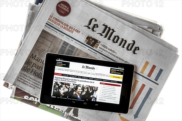 Touchscreen digital tablet showing online news on top of French Le Monde newspaper on white background
