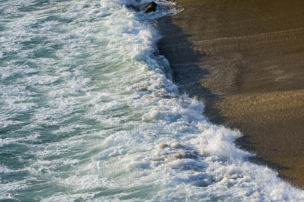 Wave in the surf crashing on sandy beach along the seashore coast