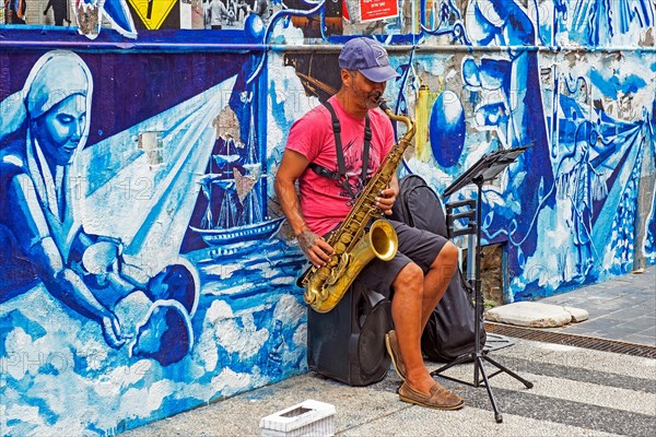 Busker playing saxophone in front of mural in the city centre of capital Montevideo