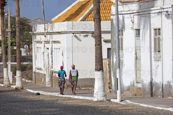 Local Creole women walking in street along white colonial buildings of the town Tarrafal on the island Santiago