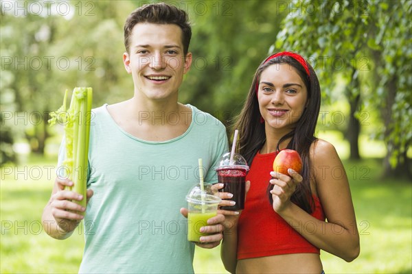 Smiling couple holding avocado apple smoothies hand