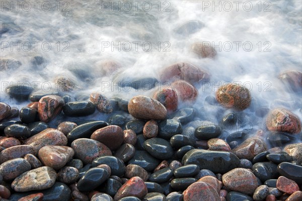 Close up of colourful pebbles covered by wave on shingle beach at rising tide