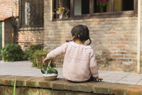 Rear view girl sitting wall holding avocado fruit small basket