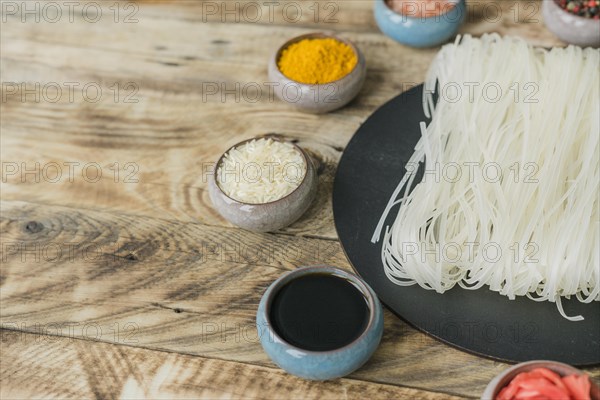 Soya sauce raw rice turmeric bowl near dried rice noodles black tray wooden texture background