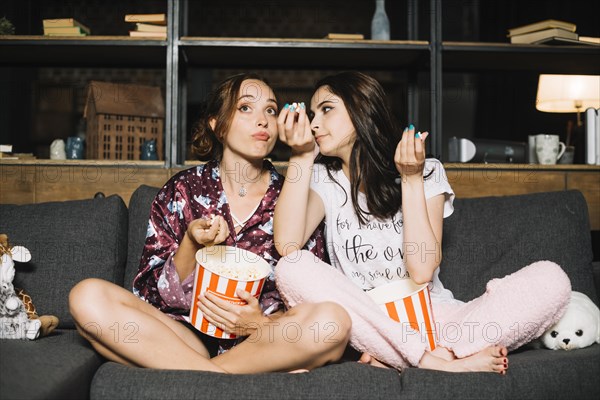 Two young women sitting sofa watching television