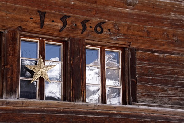Christmas decorations on window of wooden mountain cabin and reflection of snow covered mountains in the Swiss Alps