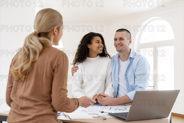 Happy embraced couple conversing with female realtor