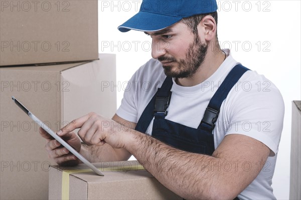 Serious courier browsing tablet near parcels