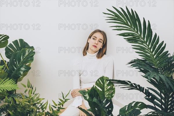 Thoughtful woman sitting floor with green plants