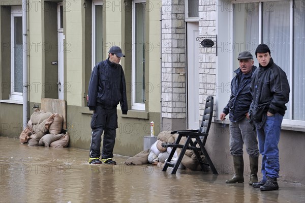 Flooded street and sandbags piled up in front of doors at Nederzwalm