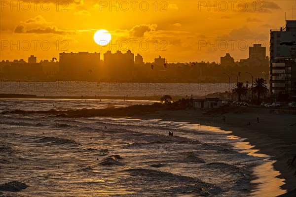 Sandy beach and surfers surfing at sunset near the city Montevideo