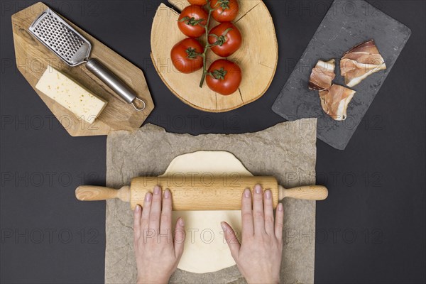 Hand rolling pizza dough parchment paper with pizza ingredient black background