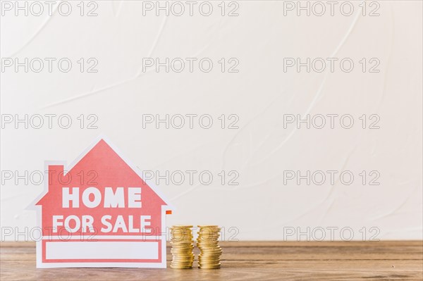 Home sale icon with stacked coins wooden desk