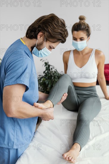 Side male osteopathic therapist with medical mask checking female patient s ankle