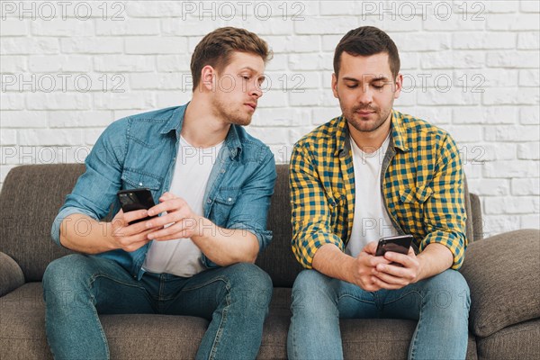 Jealous boyfriend spying his male friend watching his phone