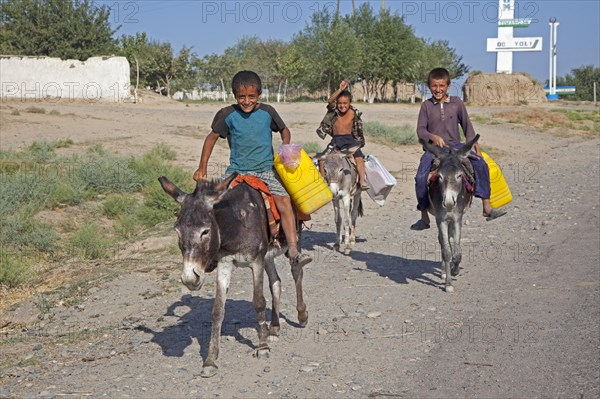 Three children riding donkeys with plastic containers to collect water
