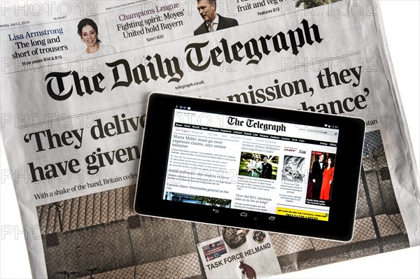 Touchscreen digital tablet showing online news on top of British The Daily Telegraph newspaper on white background