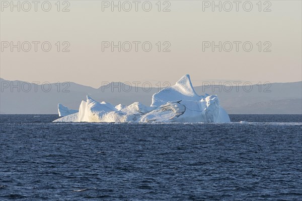 An iceberg floats in the rising morning sun off the mountains of the Greenland coast. Disko Bay