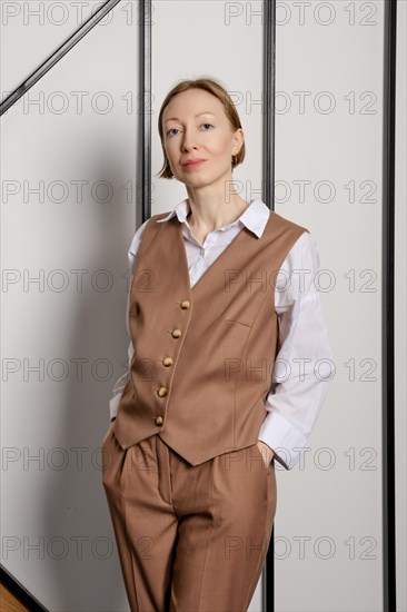 A young adult woman stands indoors with her hands in pockets