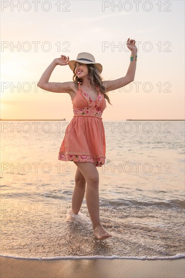 Vertical portrait of a sensual woman standing on the water of the sea during sunset