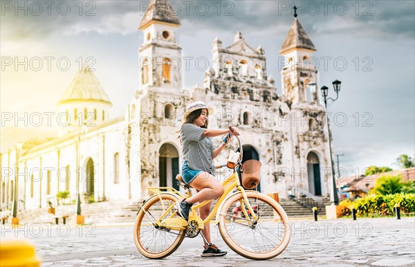 The girl is on the street smiling at the cell phone while she is on her bicycle