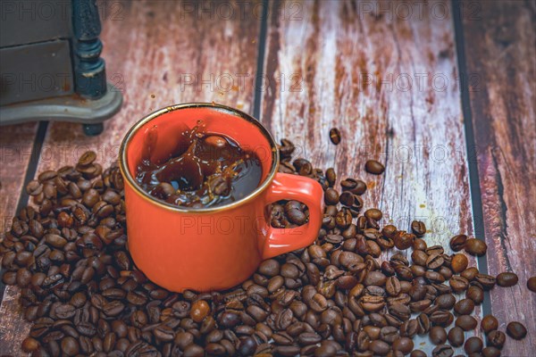 Red coffee mug with coffee beans falling inside with splash effect splash in the background a manual coffee grinder