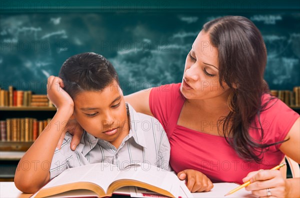 Female tutor doing homework with a young hispanic boy in the classroom