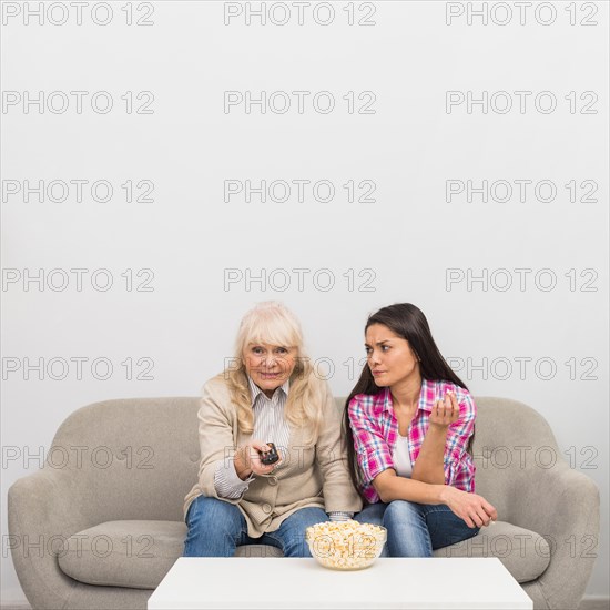 Angry daughter looking her senior mother changing channel with remote