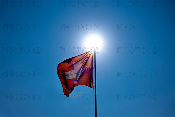 Beautiful Swiss Flag Against Blue Clear Sky and the Sun in a Windy Day in Switzerland