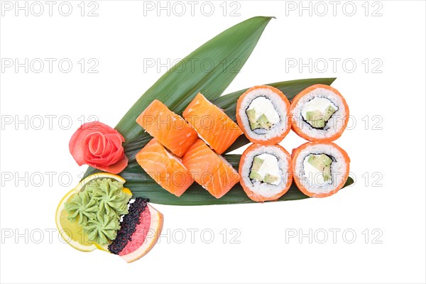 Overhead view of sushi roll with raw salmon fillet on top with avocado served on bamboo leaves