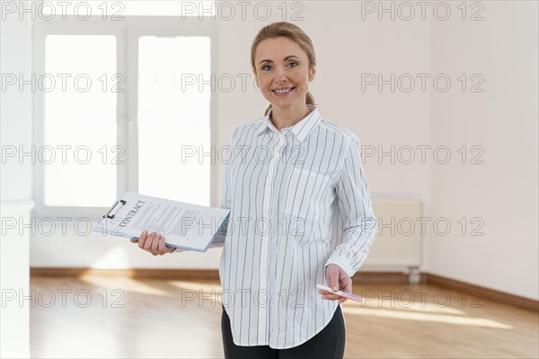 Front view smiley female realtor empty house holding clipboard