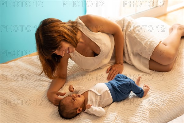 Cute baby boy resting lying on the bed with his mother in an hotel