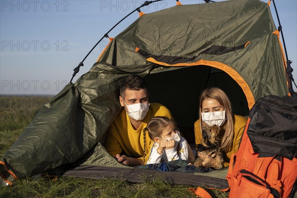 Family wearing masks sitting tent with their dog front view