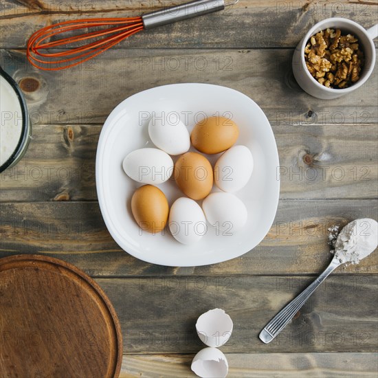 Elevated view eggs flour walnut with whisk wooden background