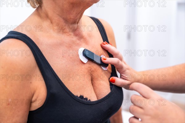 Female doctor putting unrecognizable woman with heart problems undergoing ECG Holter monitor test with innovative device on chest
