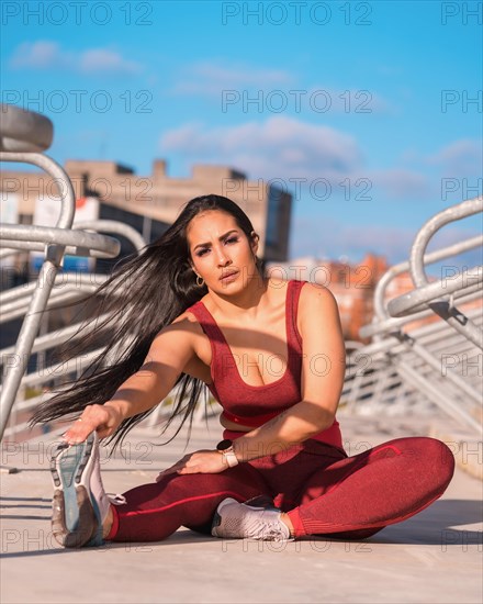 Frontal view of a woman in sports clothes sitting on a park stretching the leg